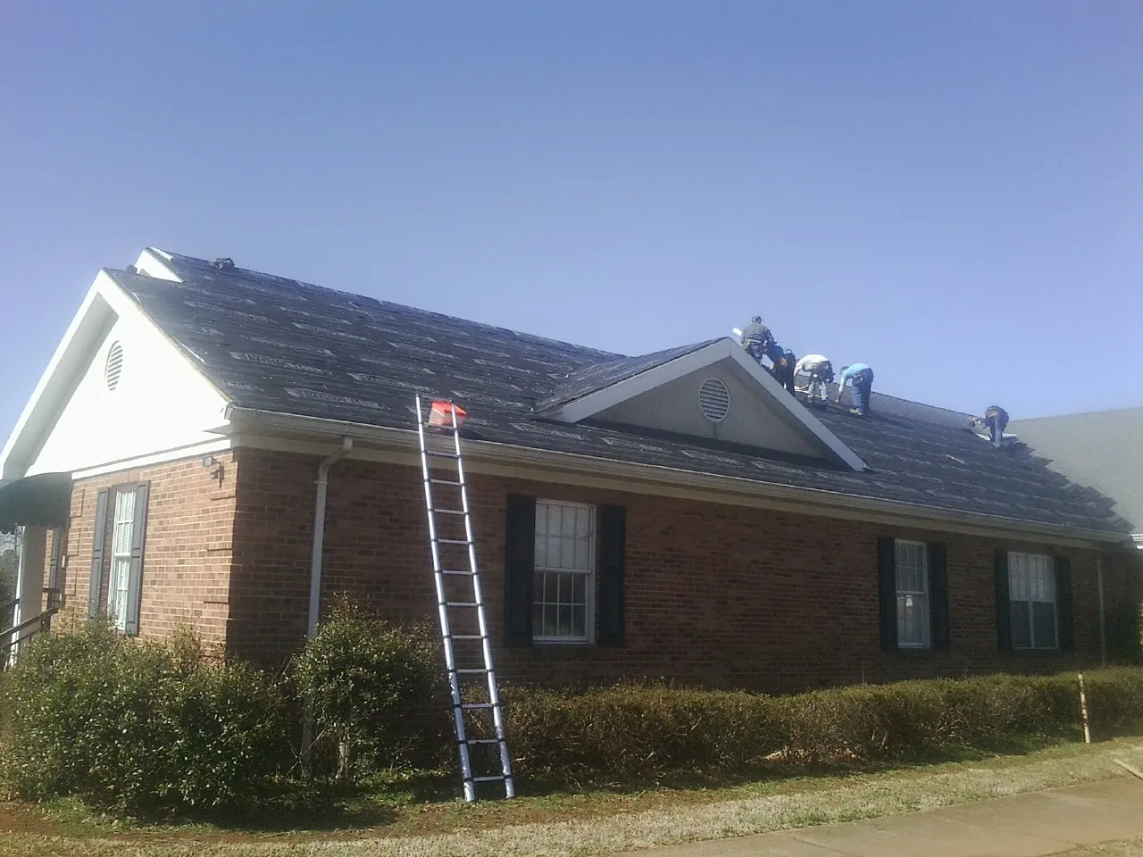 Crew tearing shingles off a brick ranch roof with a ladder set — Metal Roof Repair work by our crew in Fulton