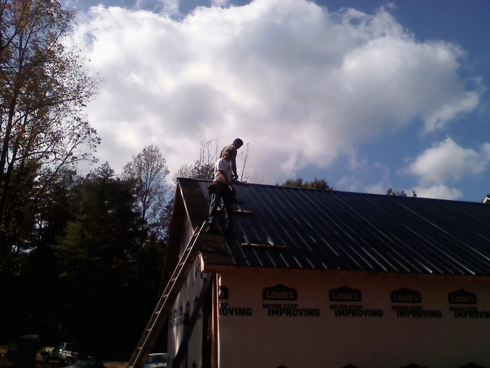 Roofer fastening dark metal panels high against a cloudy sky, from a Roof Inspection job in Fulton